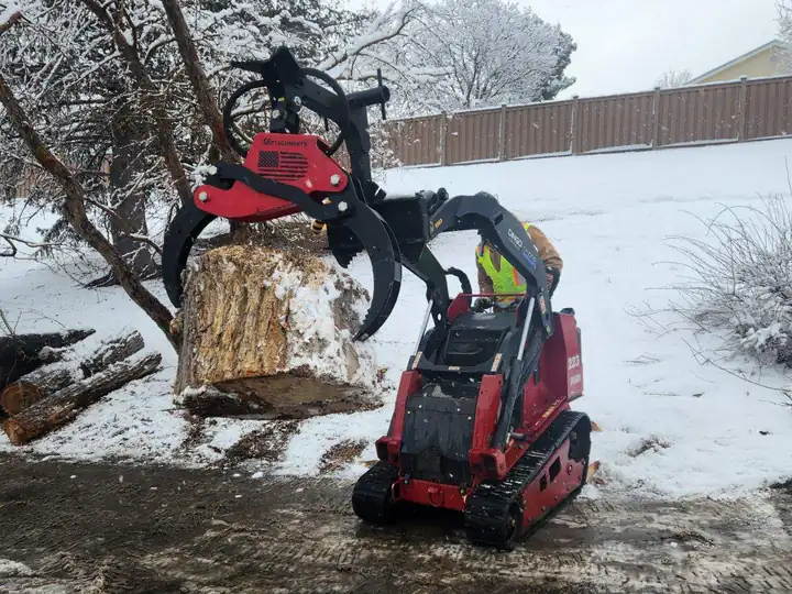 Storm damage cleanup in Larkspur, CO: compact loader moving a log in the snow after a storm