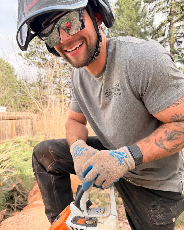 Connor Grovenor, owner of Saw and Order Tree Care in Highlands Ranch and ISA Certified Arborist, kneeling with a chainsaw