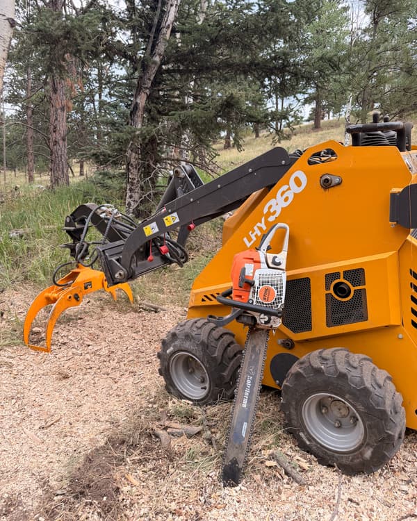 Land clearing in Colorado ponderosa forest: compact loader with a grapple and a chainsaw